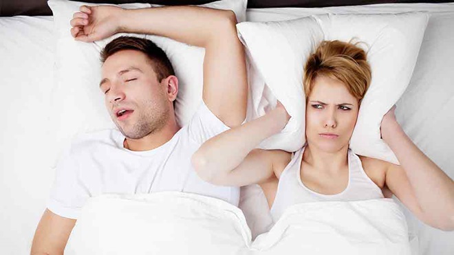 man snores while annoyed woman holds pillow over her ears